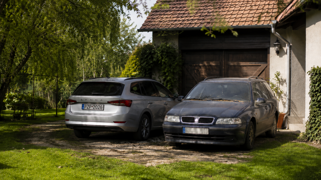 Dve autá na dvore rodinného domu — novšie používané vozidlo vedľa staršieho nepoisteného auta pokrytého prachom Zaparkované auto s úradným oznámením na čelnom skle — upozornenie na neplatné povinné zmluvné poistenie